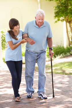 Pflegekraft unterstützt alten Mann beim Spaziergang