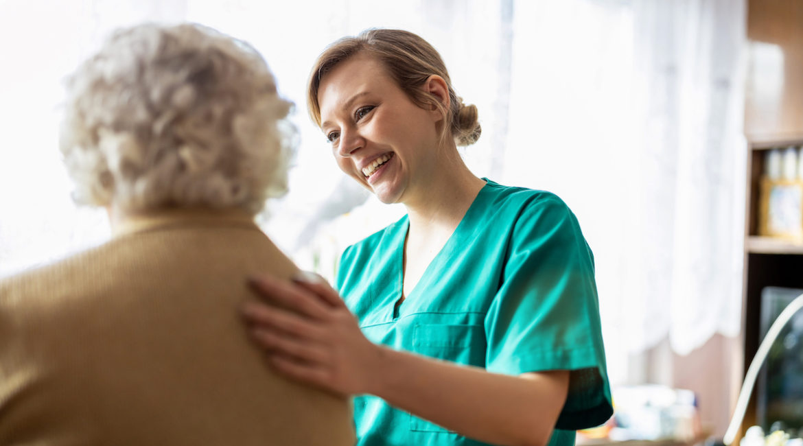 Stationäre Pflege: Altenpflegerin legt Hand auf den Rücken von Patientin