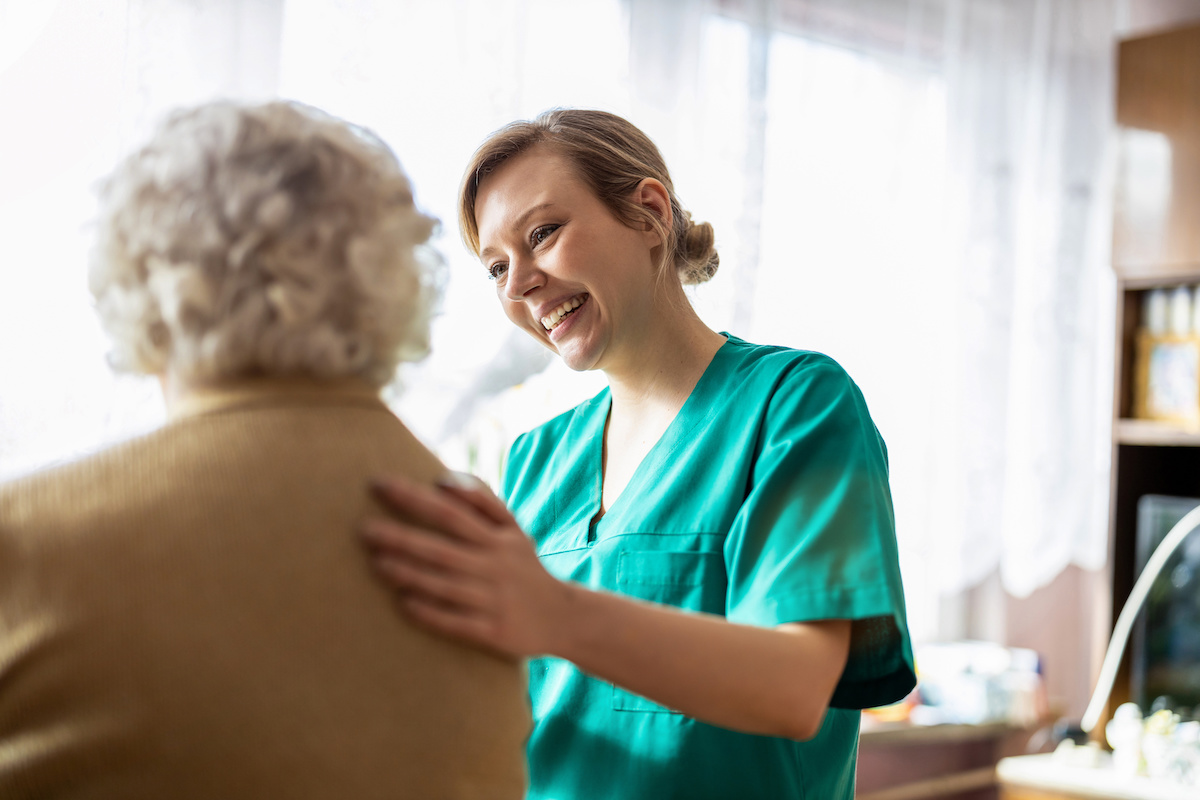 Stationäre Pflege: Altenpflegerin legt Hand auf den Rücken von Patientin