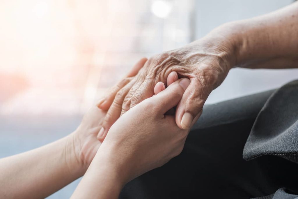 Pflegende Person hält Hand einer terminal kranken Person im Rahmen der Palliativpflege